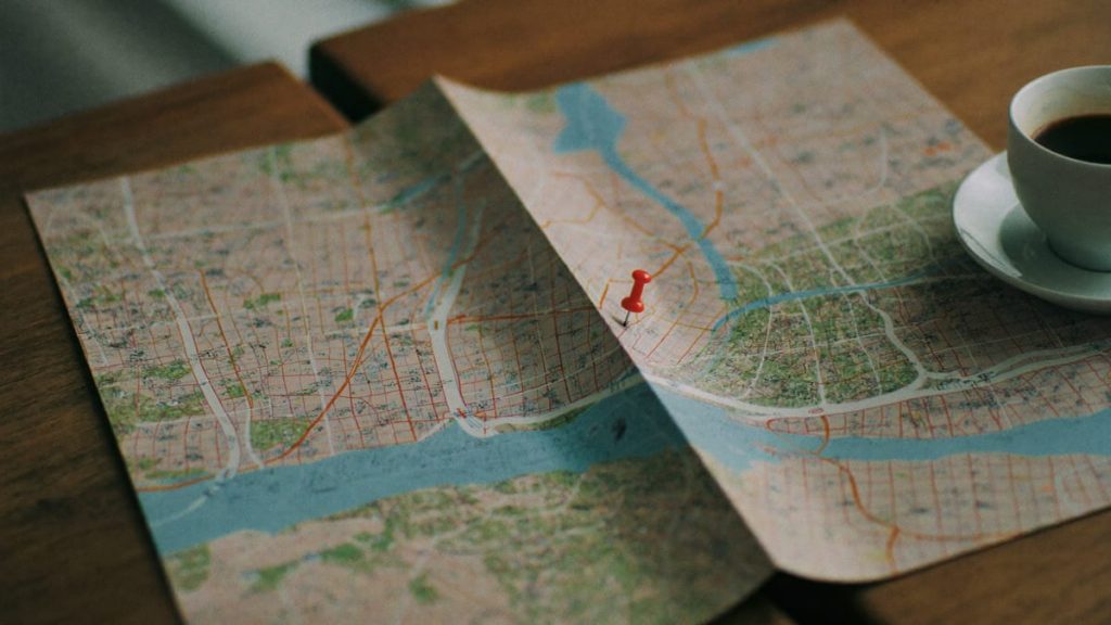 Mapa de papel con una chincheta roja marcando una ubicación junto a un café